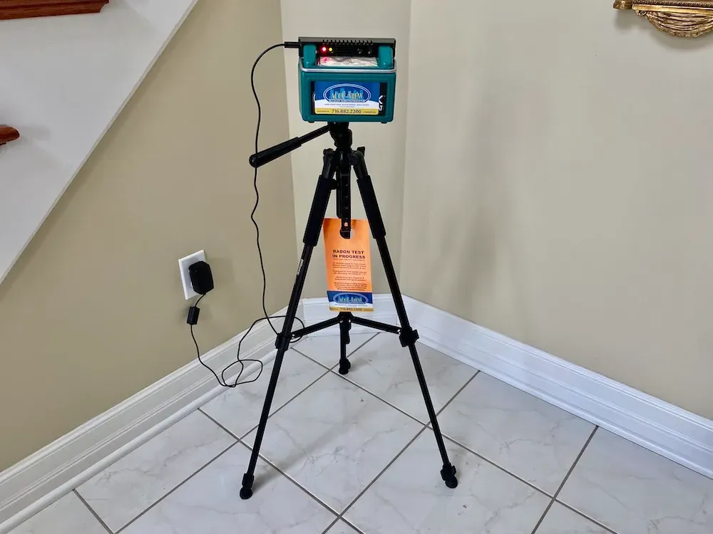 A continuous radon monitor machine set up on a black tripod inside a residential home for a radon gas inspection.